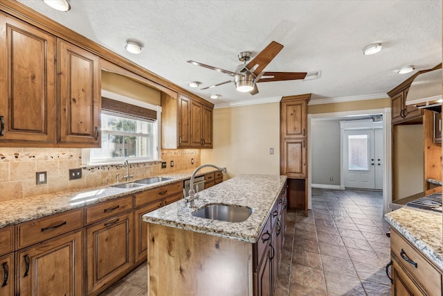 kitchen featuring a sink, tasteful backsplash, a center island with sink, and brown cabinetry