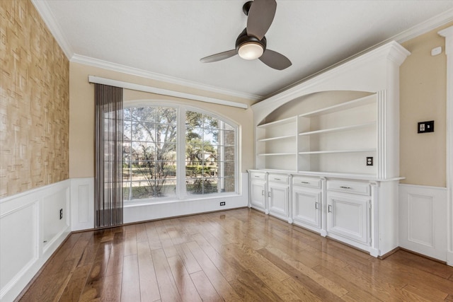 empty room featuring wainscoting, ornamental molding, ceiling fan, and hardwood / wood-style flooring