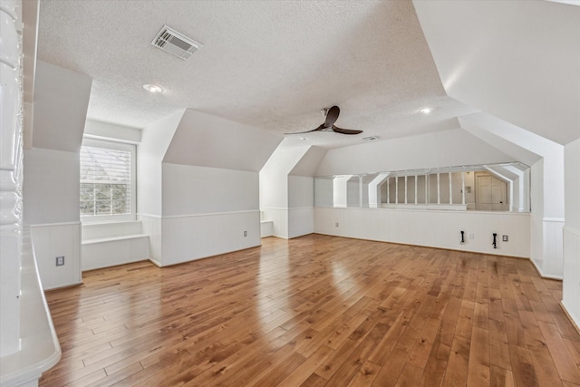 additional living space with vaulted ceiling, visible vents, a textured ceiling, and hardwood / wood-style floors