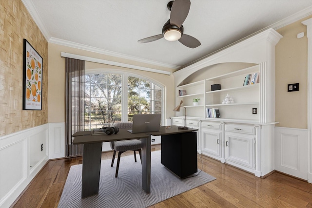 office featuring a wainscoted wall, wood-type flooring, ceiling fan, and ornamental molding