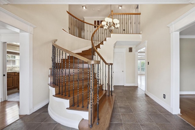 stairway with a notable chandelier, baseboards, a towering ceiling, and ornamental molding