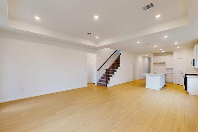 unfurnished living room with visible vents, a sink, light wood-style flooring, and stairs