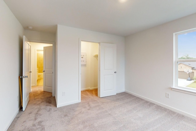 unfurnished bedroom with light carpet, a closet, a walk in closet, and baseboards