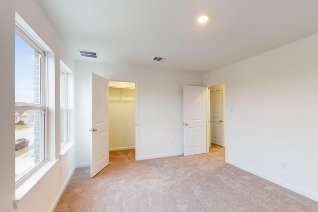 unfurnished bedroom with light carpet, baseboards, visible vents, and a walk in closet