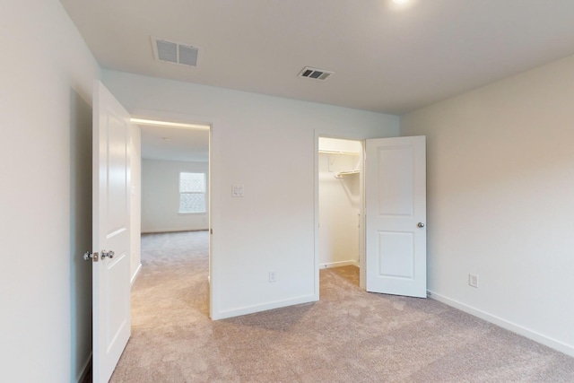 unfurnished bedroom with a walk in closet, visible vents, light carpet, and baseboards