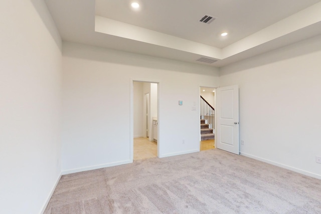 unfurnished room with stairs, a tray ceiling, visible vents, and baseboards