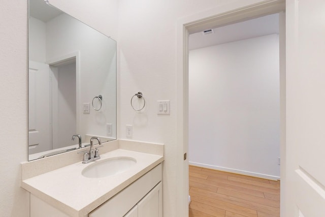 bathroom with visible vents, vanity, baseboards, and wood finished floors