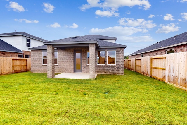 rear view of property with a lawn, a fenced backyard, roof with shingles, a patio area, and brick siding