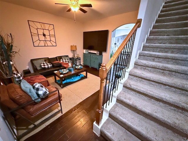 living area with arched walkways, ceiling fan, wood finished floors, and stairs