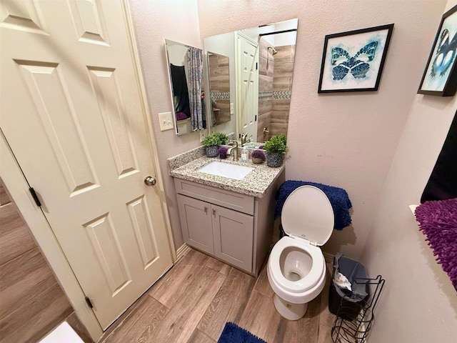 full bathroom featuring toilet, wood finish floors, a tile shower, and vanity