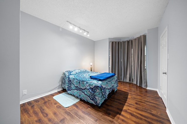 bedroom with track lighting, a textured ceiling, baseboards, and wood finished floors