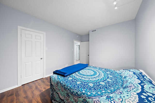 bedroom featuring a textured ceiling, wood finished floors, visible vents, and baseboards