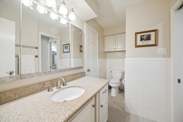 bathroom with toilet, a wainscoted wall, tile patterned floors, vanity, and tile walls