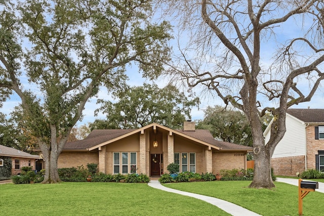 mid-century modern home with roof with shingles, brick siding, a chimney, and a front lawn