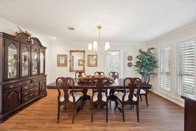 dining space with an inviting chandelier, crown molding, visible vents, and wood finished floors