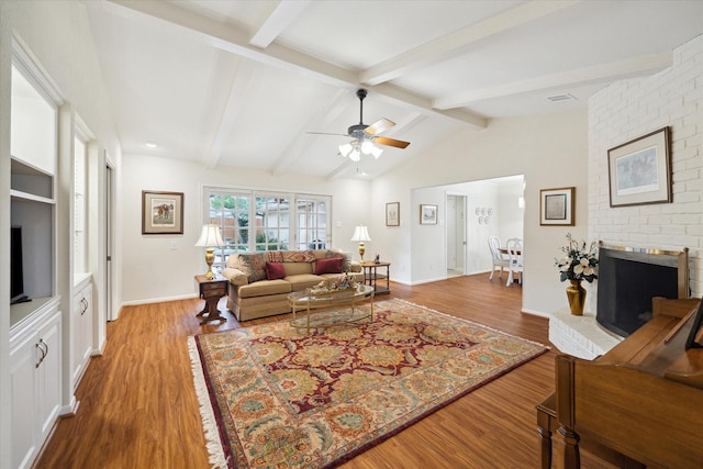 living area with a fireplace, vaulted ceiling with beams, a ceiling fan, wood finished floors, and baseboards