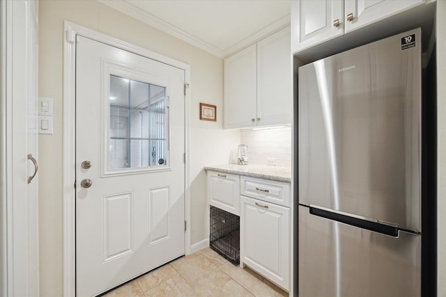 kitchen featuring tasteful backsplash, white cabinets, freestanding refrigerator, light stone countertops, and crown molding