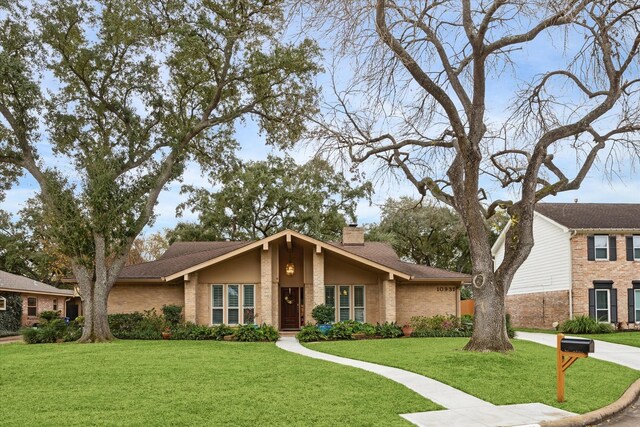 mid-century home with roof with shingles, brick siding, a chimney, and a front yard