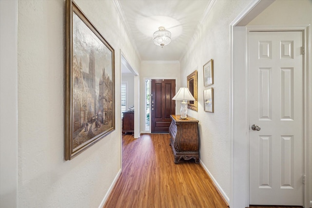 corridor featuring ornamental molding, a textured wall, baseboards, and wood finished floors