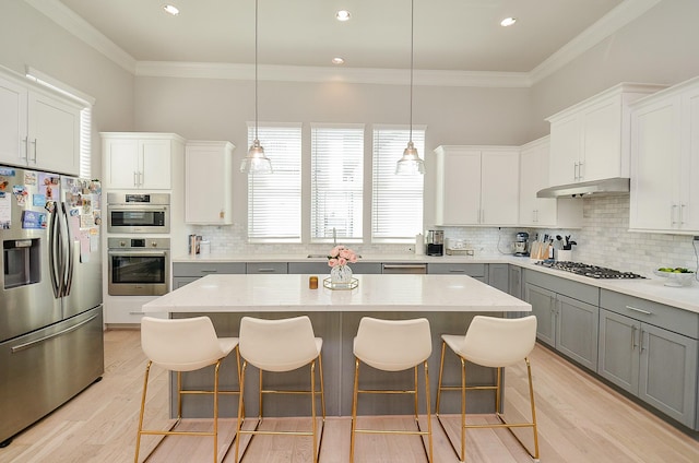 kitchen featuring crown molding, gray cabinetry, appliances with stainless steel finishes, light wood-style floors, and under cabinet range hood