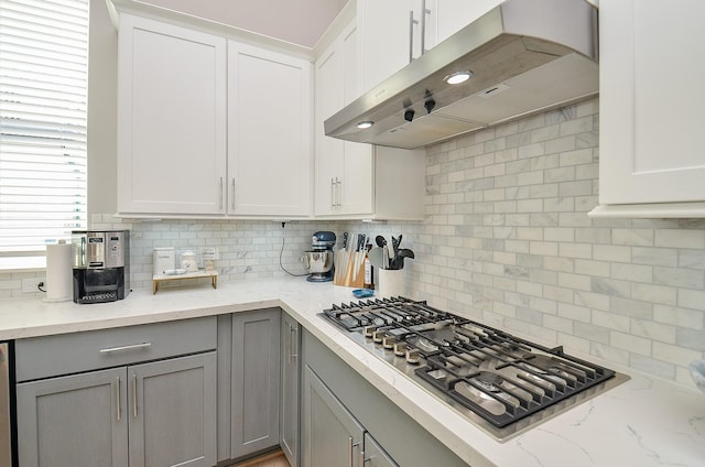 kitchen featuring gray cabinetry, stainless steel gas cooktop, under cabinet range hood, white cabinets, and decorative backsplash