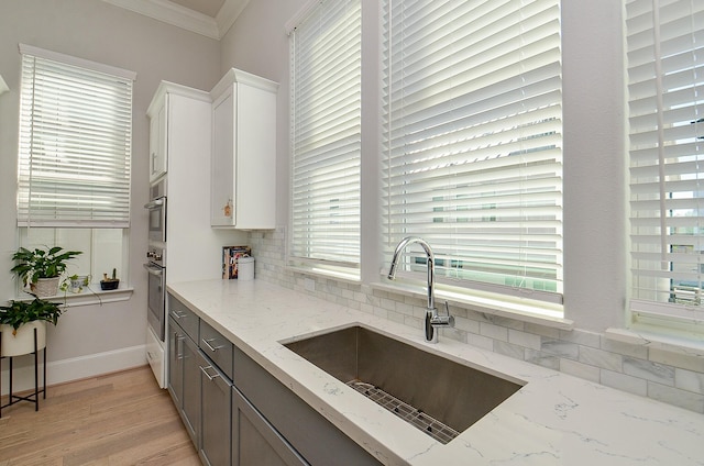 kitchen with a sink, light stone countertops, crown molding, stainless steel oven, and backsplash