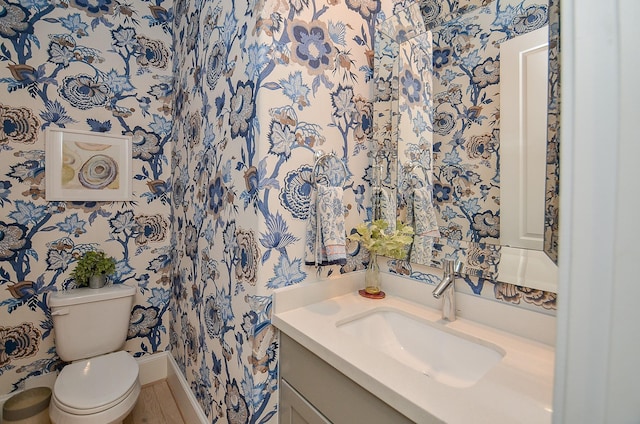 bathroom with toilet, vanity, and wallpapered walls