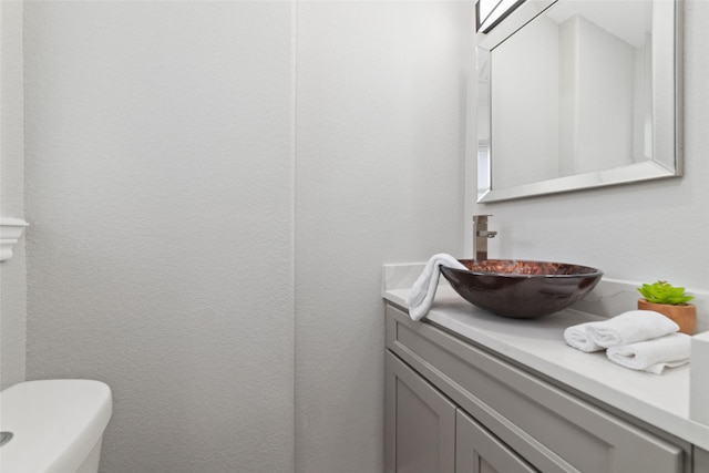 bathroom featuring toilet, a textured wall, and vanity