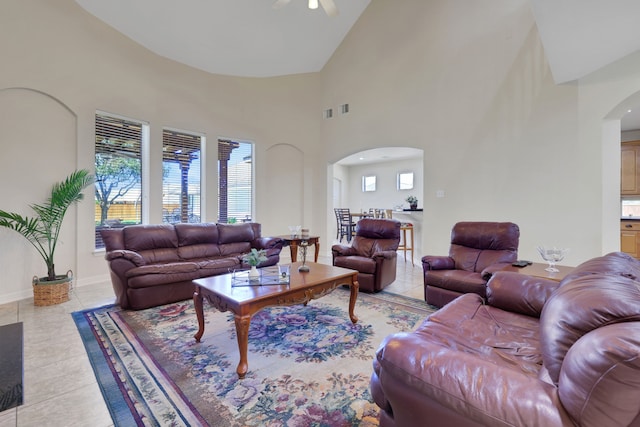 living area featuring arched walkways, light tile patterned floors, a ceiling fan, and baseboards