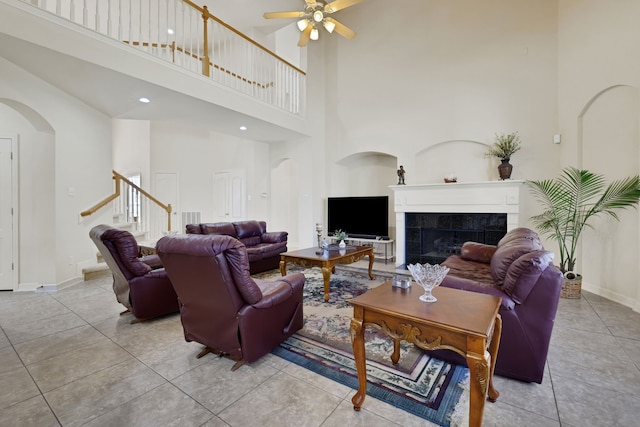 tiled living room with arched walkways, a fireplace, stairway, a ceiling fan, and baseboards