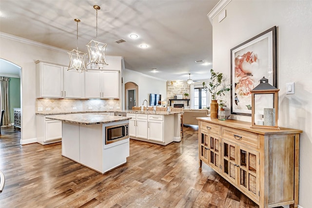 kitchen featuring arched walkways, a peninsula, a kitchen island, visible vents, and stainless steel microwave