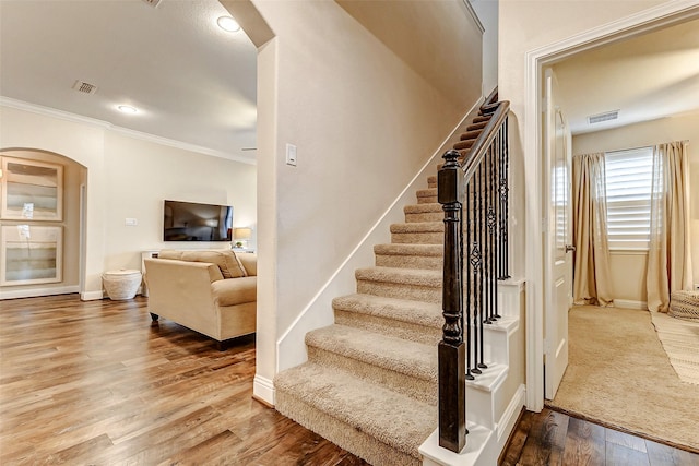 staircase featuring arched walkways, crown molding, visible vents, wood finished floors, and baseboards