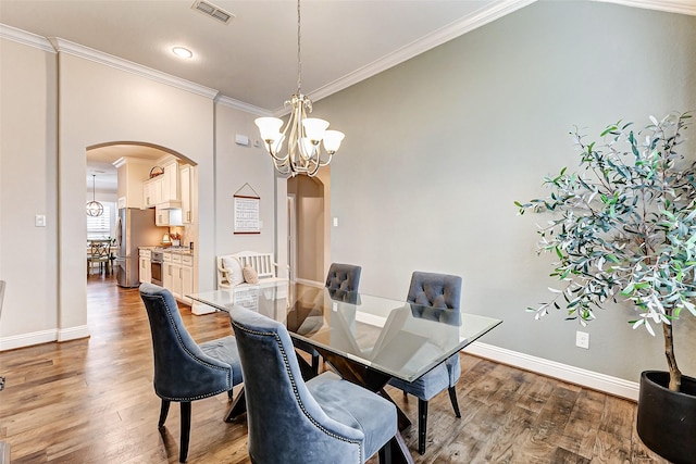 dining space with arched walkways, visible vents, ornamental molding, wood finished floors, and a chandelier