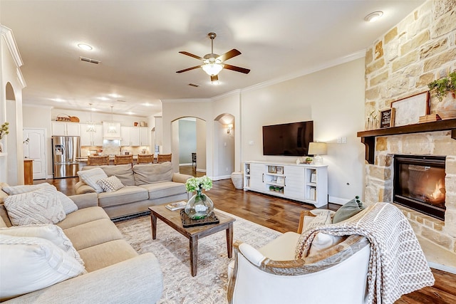 living area with arched walkways, visible vents, crown molding, and wood finished floors