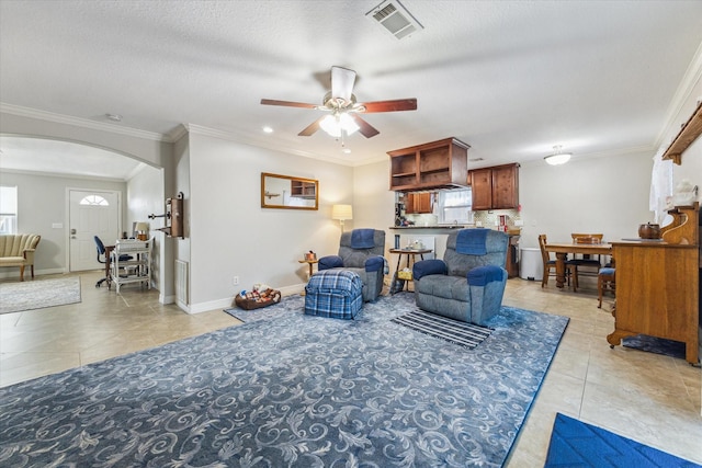 living area with arched walkways, light tile patterned floors, visible vents, baseboards, and crown molding