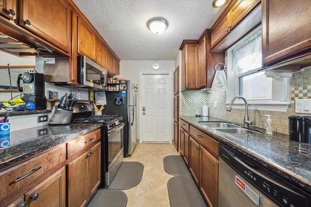 kitchen with light tile patterned floors, decorative backsplash, dark stone counters, appliances with stainless steel finishes, and a sink