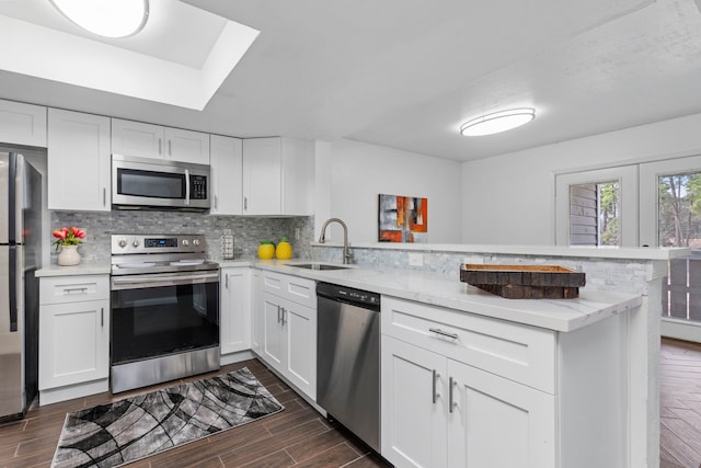 kitchen featuring stainless steel appliances, a peninsula, wood finish floors, a sink, and backsplash