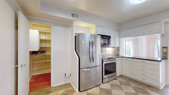 kitchen featuring tasteful backsplash, visible vents, white cabinets, dark countertops, and stainless steel appliances