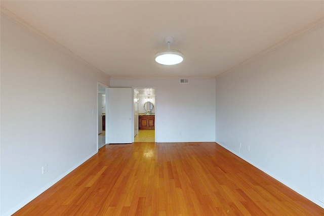 spare room with baseboards, light wood-type flooring, visible vents, and crown molding