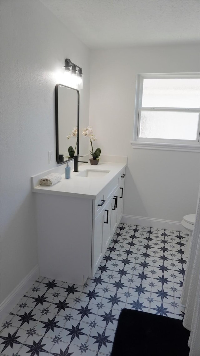 bathroom with toilet, vanity, baseboards, and tile patterned floors