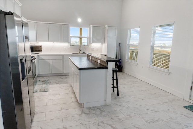 kitchen featuring a breakfast bar area, a sink, marble finish floor, appliances with stainless steel finishes, and plenty of natural light