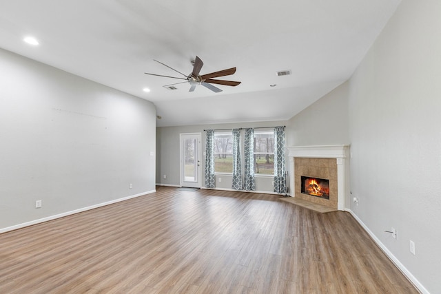 unfurnished living room featuring ceiling fan, a fireplace, wood finished floors, visible vents, and vaulted ceiling