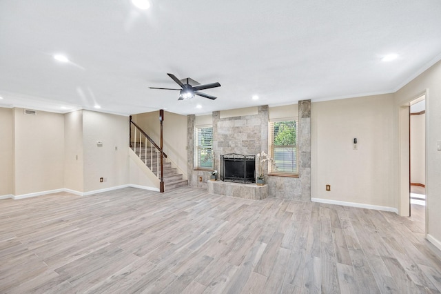 unfurnished living room with light wood finished floors, baseboards, ceiling fan, stairs, and a stone fireplace