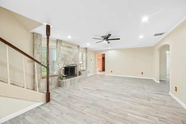 unfurnished living room with light wood finished floors, visible vents, arched walkways, a ceiling fan, and a tiled fireplace