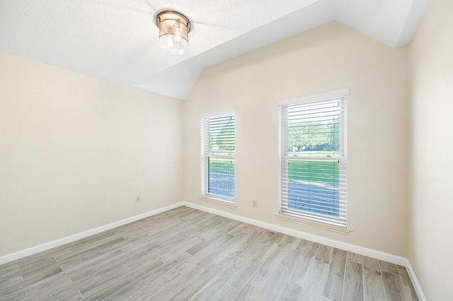 empty room with vaulted ceiling, light wood-style flooring, and baseboards