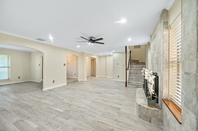 unfurnished living room featuring arched walkways, ornamental molding, stairway, and visible vents