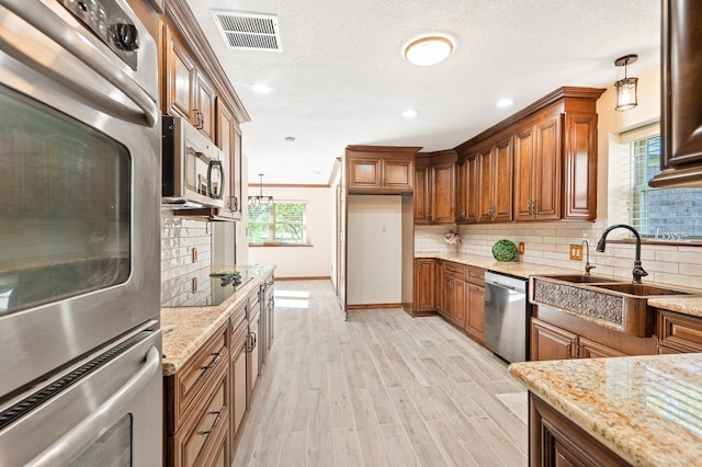 kitchen with a sink, visible vents, appliances with stainless steel finishes, backsplash, and brown cabinetry