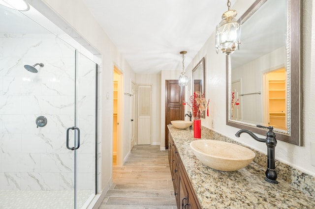 bathroom featuring double vanity, wood finished floors, a stall shower, and a sink