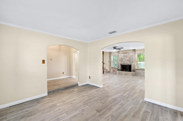 empty room with arched walkways, a fireplace, visible vents, wood finished floors, and baseboards