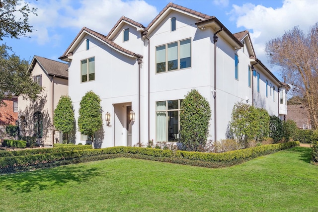 rear view of house featuring stucco siding, a tiled roof, and a yard